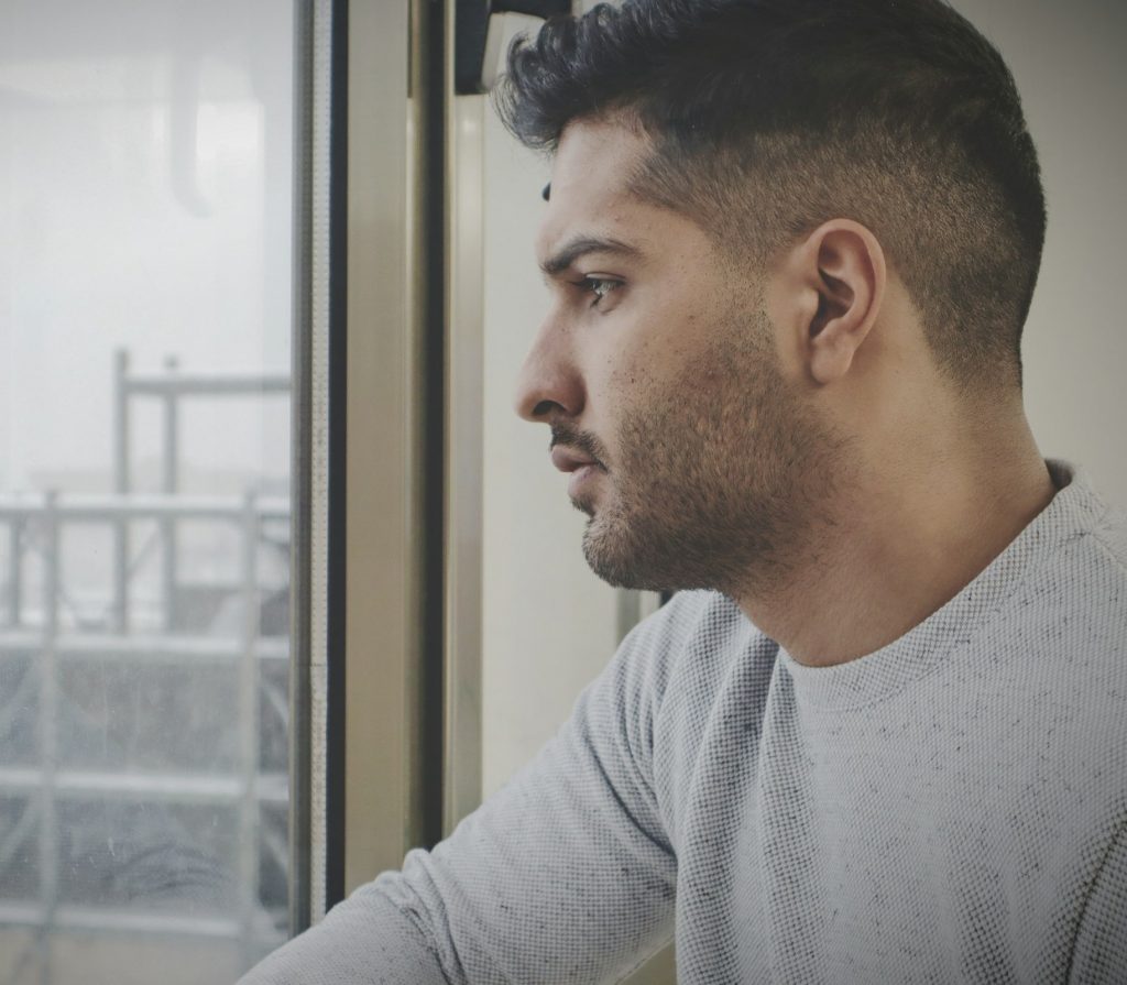 Mann blickt nachdenklich aus dem Fenster und wirkt in Gedanken vertieft